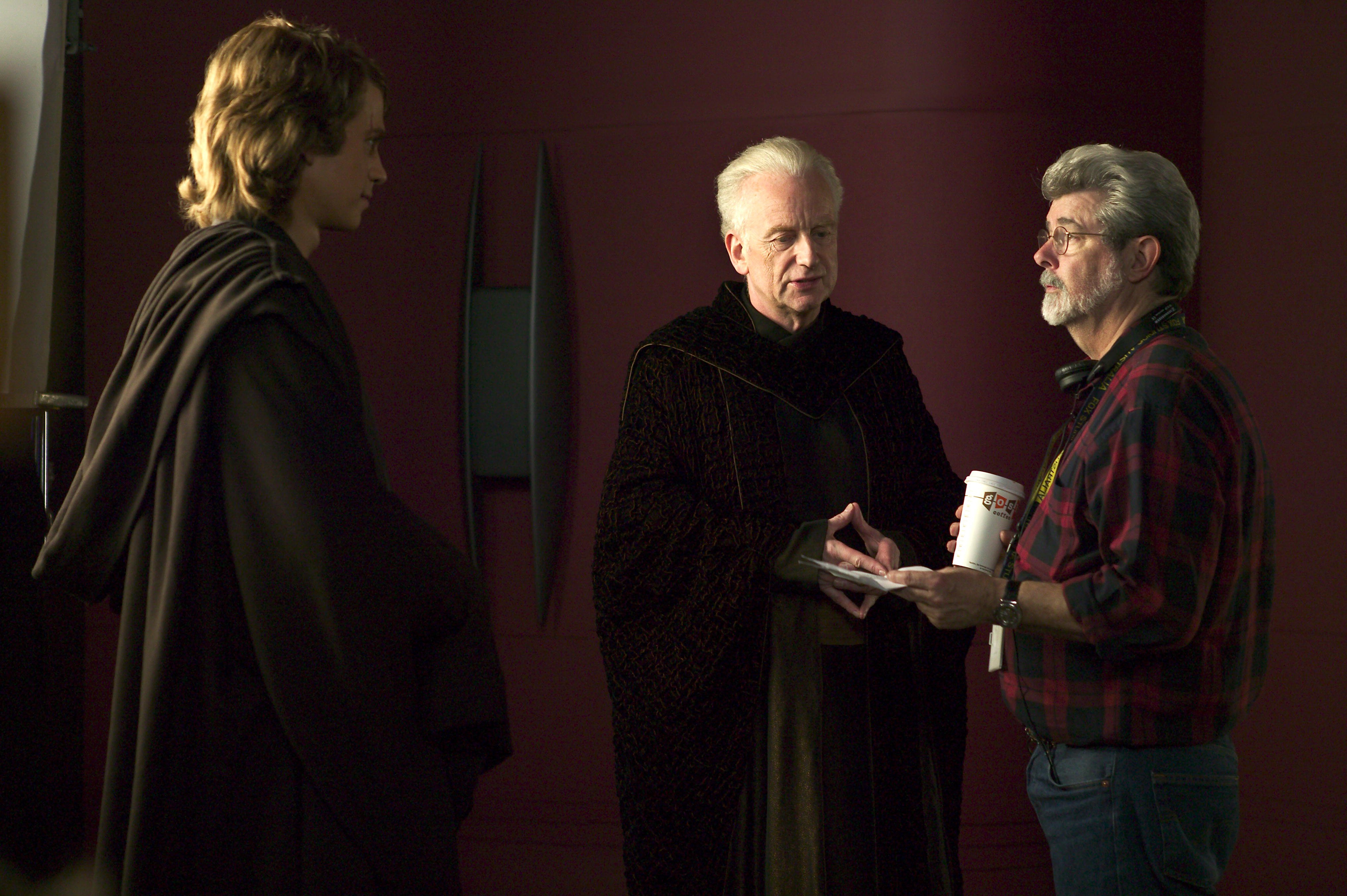 Actors Hayden Christensen (Anakin Skywalker) and Ian McDiarmid (Supreme Chancellor Palpatine) discuss a major scene in the Supreme Chancellor's office with director George Lucas. Photo by Merrick Morton.TM & © 2005 Lucasfilm Ltd. All Rights Reserved. Photo by Merrick Morton.